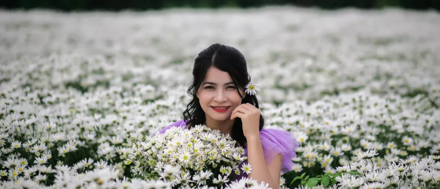 Frau sitzt lächelnd in einer Wiese mit weissen Blumen